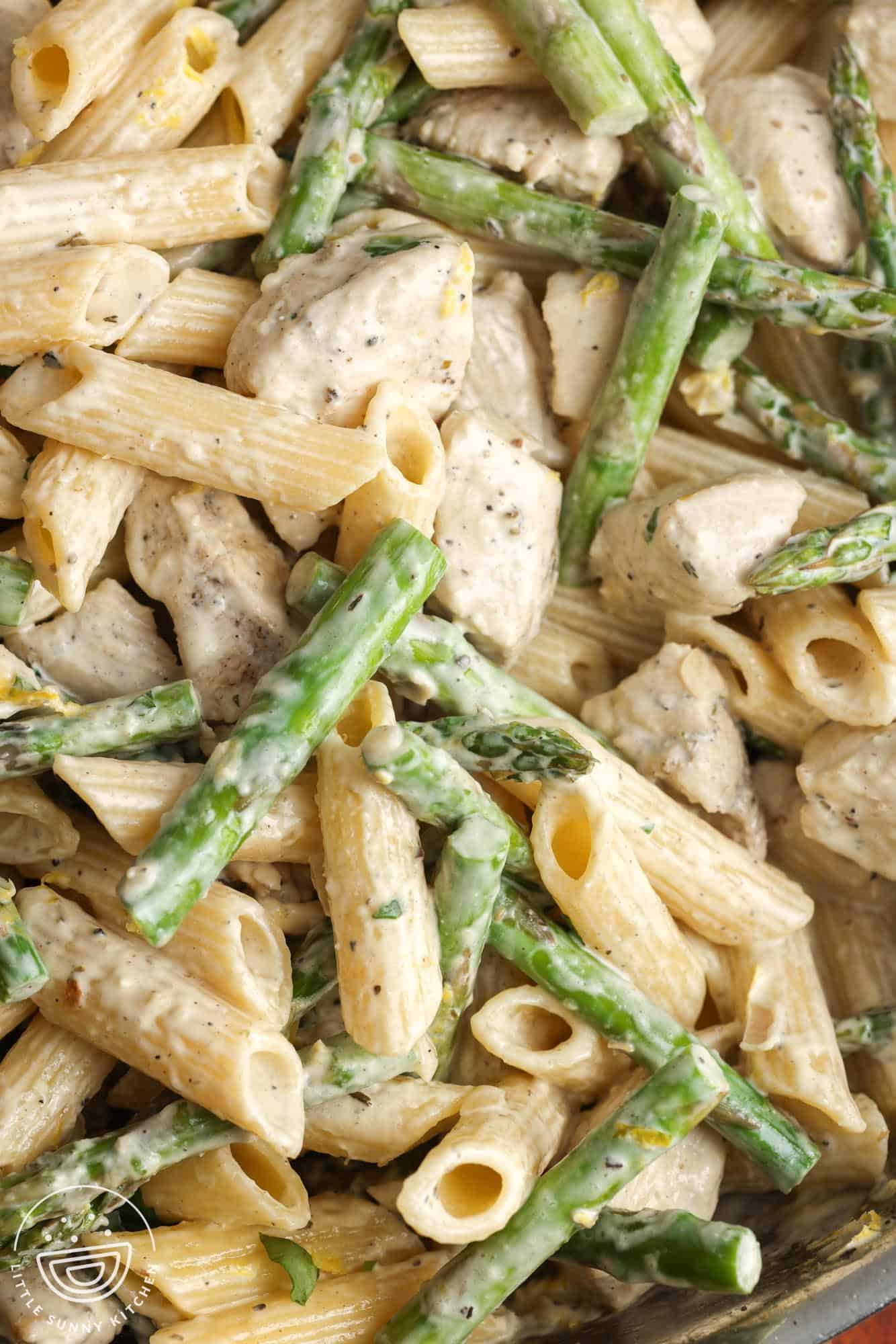 Closeup of diced chicken and asparagus mixed with penne pasta and a creamy sauce.