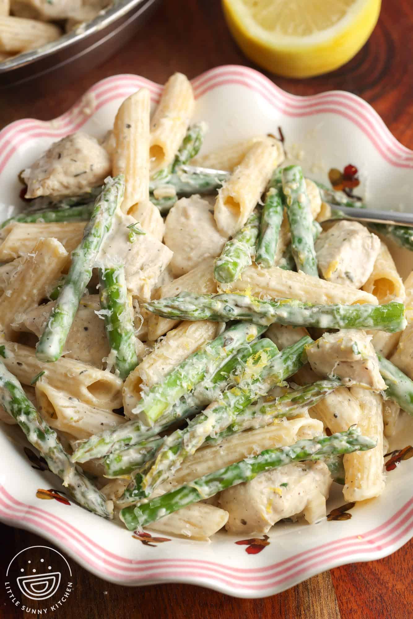 a pink striped fluted bowl holding a serving of chicken asparagus pasta, garnished with parmesan cheese and lemon zest.