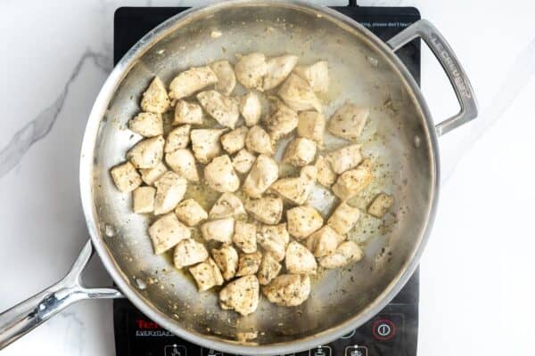 diced chicken breast, seasoned, cooking in a stainless steel skillet over an electric single burner.
