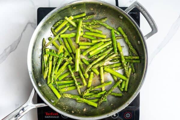 chopped asparagus spears cooking in a stainless steel skillet.