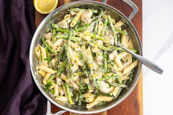 creamy chicken and asparagus pasta in a skillet, garnished with parmesan and lemon zest.
