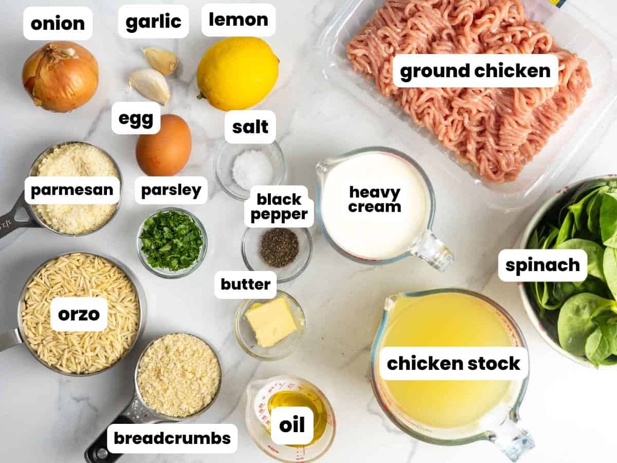 Ingredients for making ground chicken meatballs seasoned with lemon, garlic, onion, and parsley, as well as orzo, spinach, and parmesan cheese. All ingredients are measured into small bowls and arranged on a marble counter.