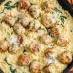 a frying pan of creamy orzo pasta with spinach and chicken meatballs, set on a wooden cutting board, garnished with parmesan cheese.