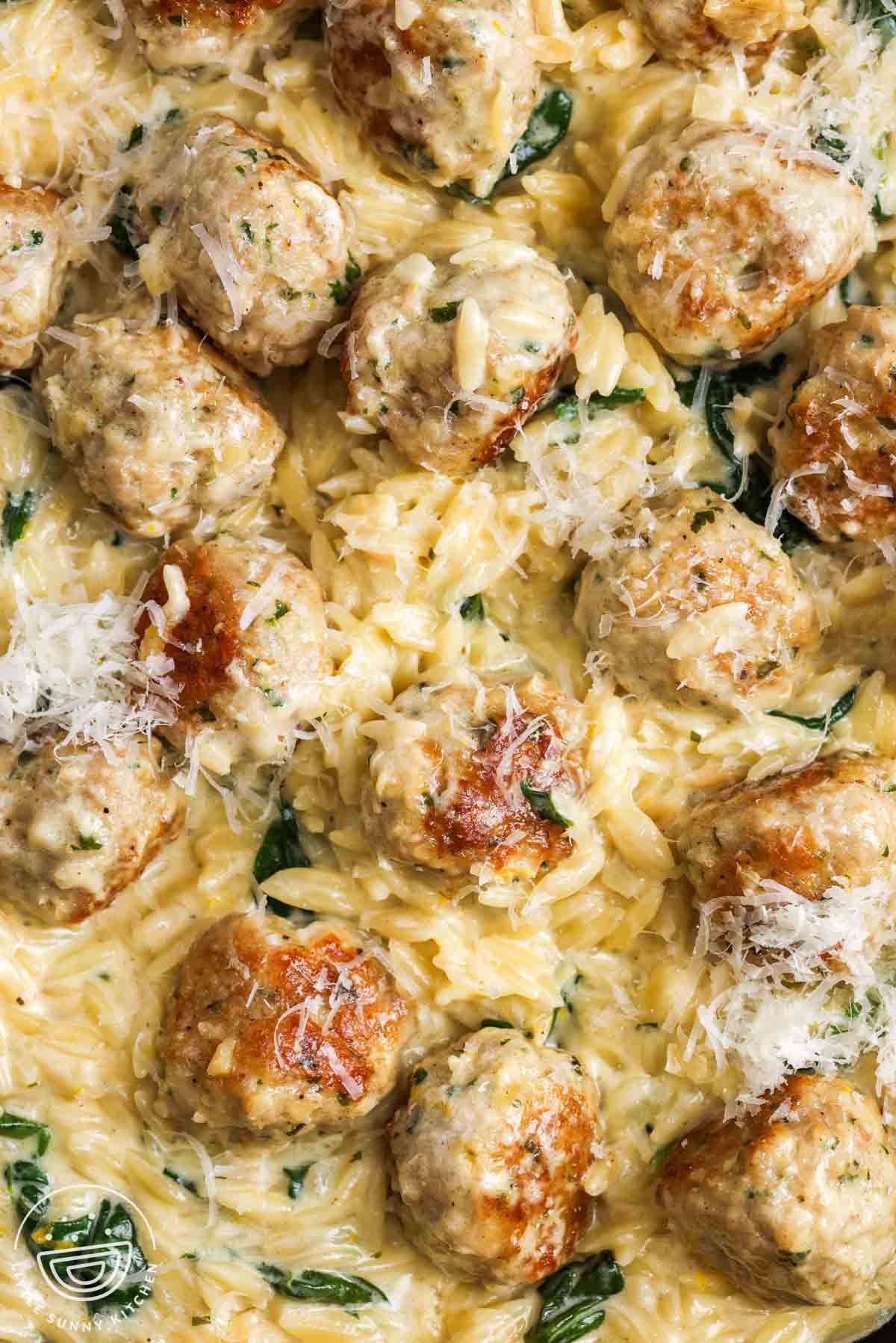 closeup of a one pan meal of creamy orzo with chicken meatballs and spinach.