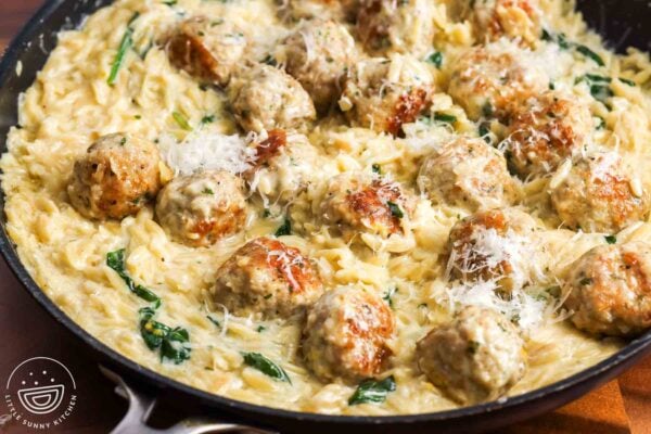 closeup of chicken meatballs with creamy lemon orzo and spinach in a skillet, garnished with parmesan cheese.