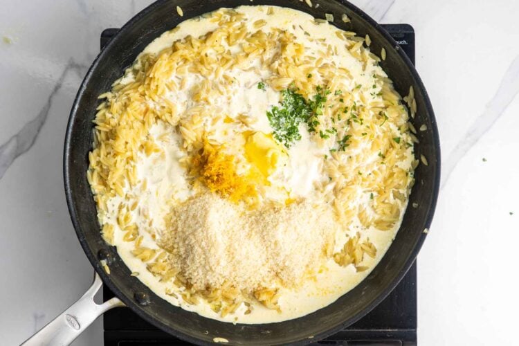 cream, butter, parmesan cheese, and lemon zest added to finish a skillet of orzo that has been cooked in chicken broth.
