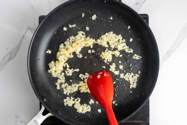 diced onion cooking in a nonstick pan, stirred with a red spatula.