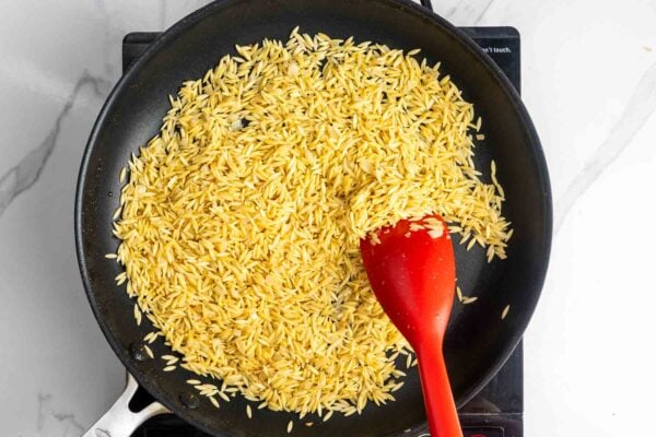 Orzo toasting in a skillet with sauteed onion.