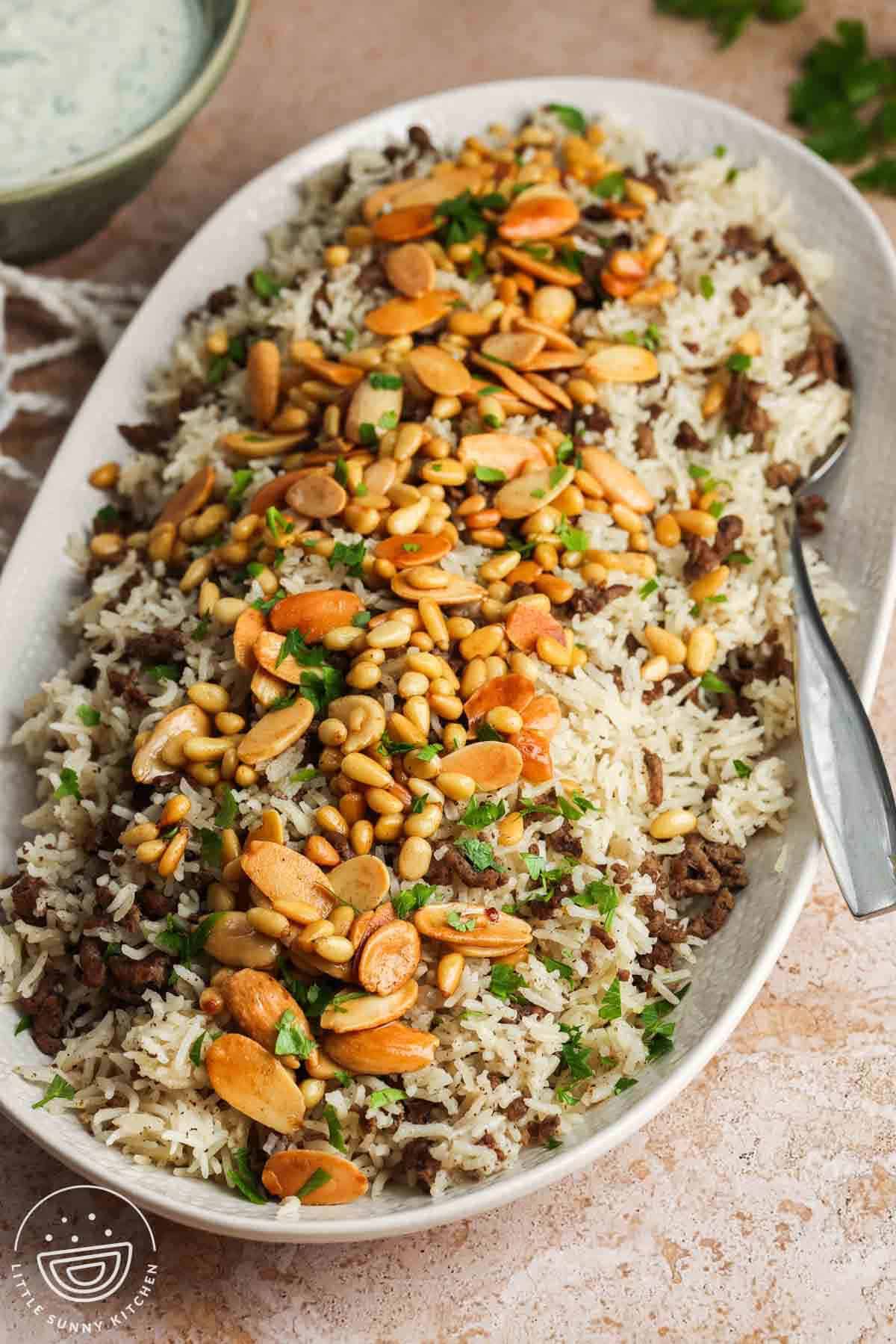 An oval platter of Hashweh spiced beef and rice topped with toasted nuts.