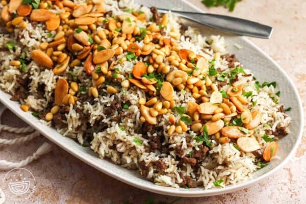 A long oval platter of fluffy Lebanese rice with spiced ground beef, topped with fresh herbs and toasted nuts.