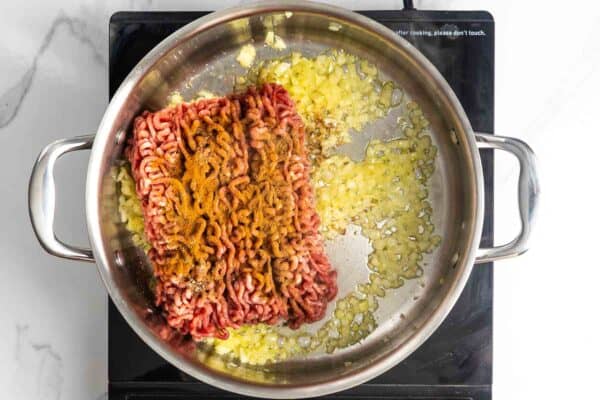 Seasoned raw ground beef added to sauteed onions in a pan.