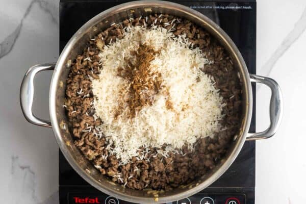 basmati rice and baharat seasoning added to a pan of cooked ground beef.