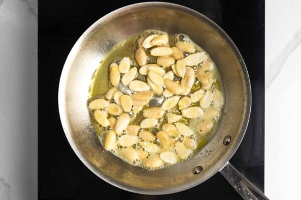 blanched almond halves toasting in oil in a small frying pan.