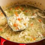 A red Dutch oven filled with lemon chicken orzo soup, featuring shredded chicken, tender orzo pasta, diced carrots, celery, and fresh dill, with a ladle scooping up a hearty portion.