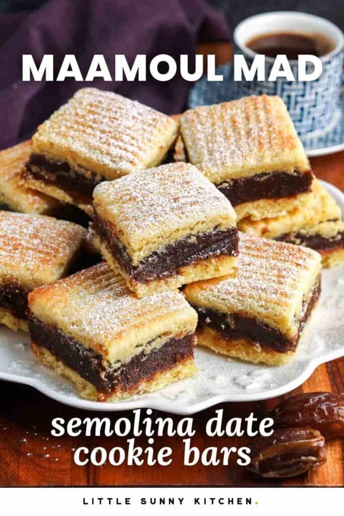 Stacked Maamoul Mad semolina cookie bars filled with date paste and dusted with powdered sugar, served on a white plate with whole dates and a cup of coffee in the background.