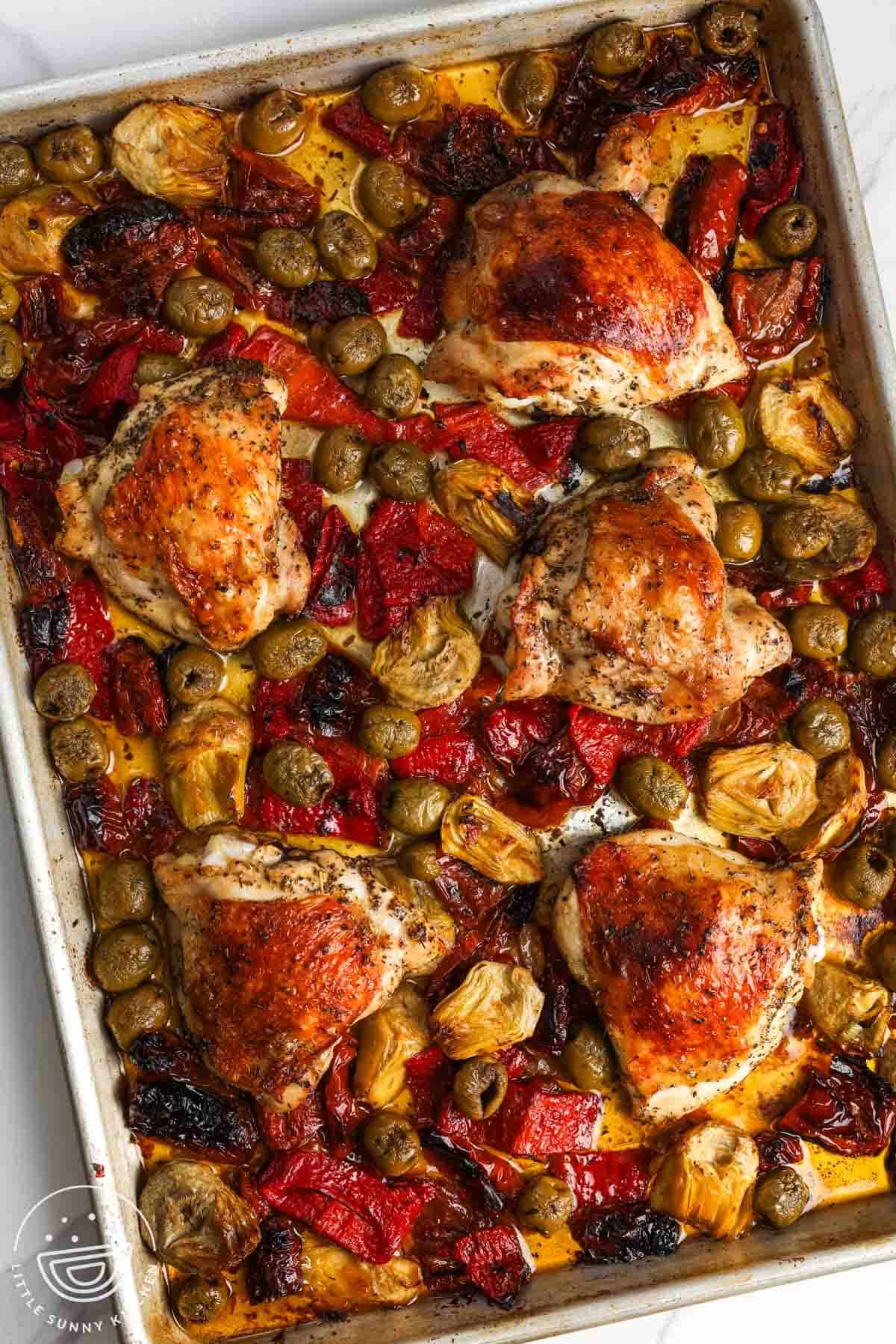 a sheet pan dinner of roasted chicken thighs, olives, artichokes, and roasted red peppers.