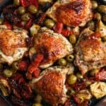 Crispy bone in chicken thighs baked with olives and red peppers, on a black rectangular platter.