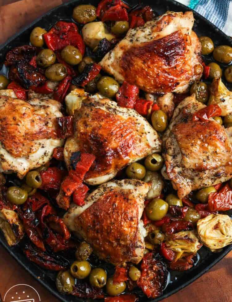 Crispy bone in chicken thighs baked with olives and red peppers, on a black rectangular platter.