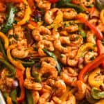 Sheet pan shrimp fajitas still in the pan, garnished with chopped herbs.