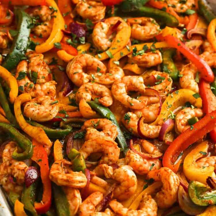 Sheet pan shrimp fajitas still in the pan, garnished with chopped herbs.