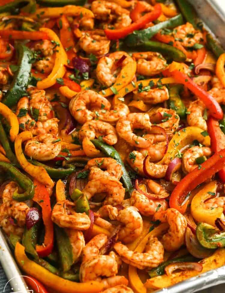 Sheet pan shrimp fajitas still in the pan, garnished with chopped herbs.