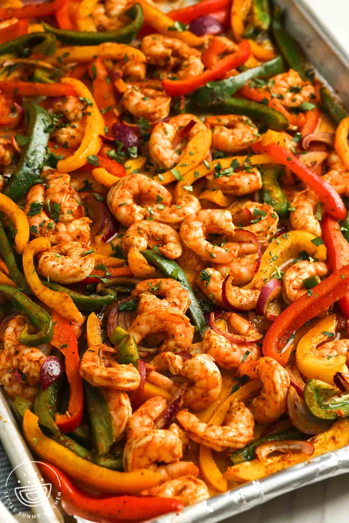 Sheet pan shrimp fajitas still in the pan, garnished with chopped herbs.