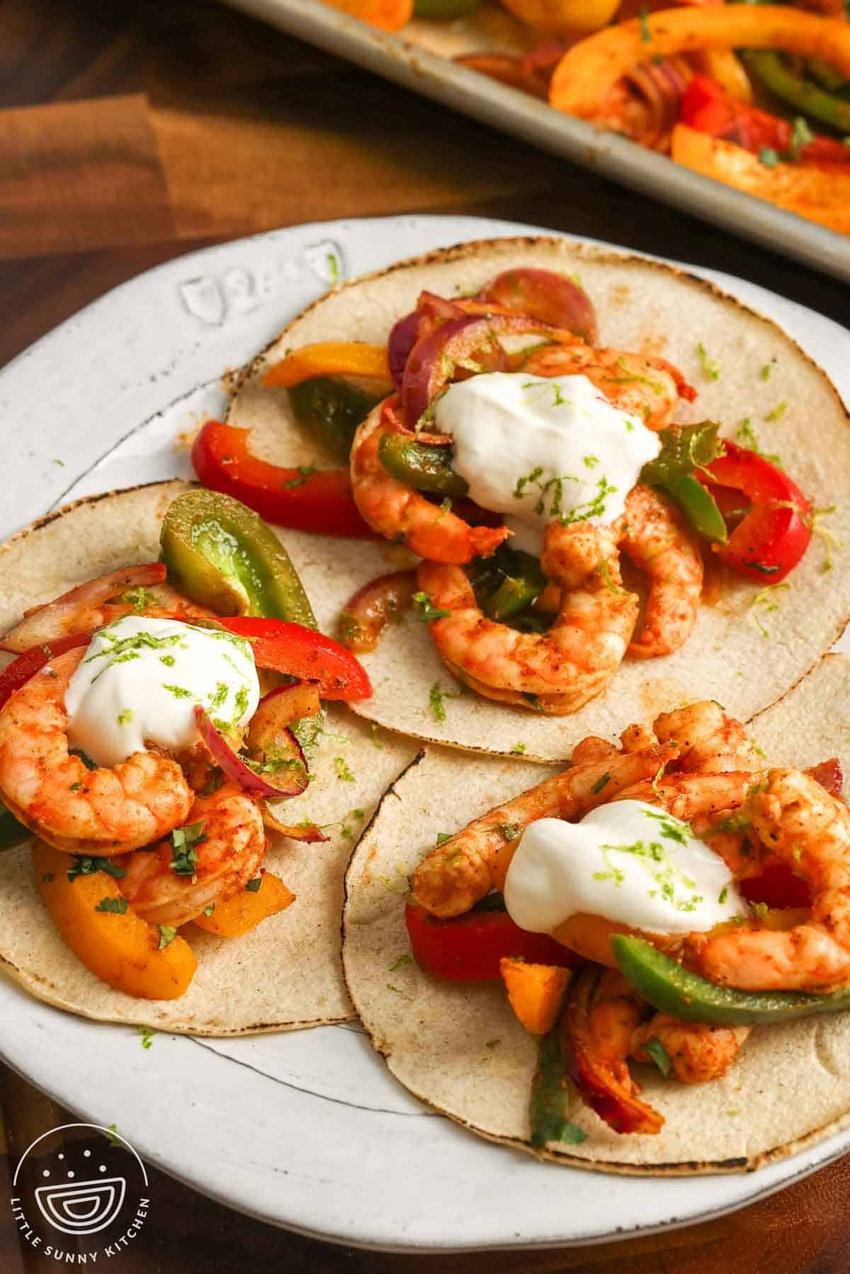 Three shrimp fajitas made on toasted tortillas, topped with sour cream and lime zest.