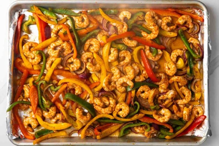 Cooked sheet pan shrimp fajitas, including peppers and onions, on a foil lined pan.