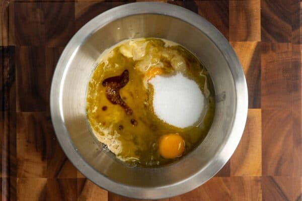 mashed banana in a metal mixing bowl with oil, sugar, egg, vanilla and tahini.