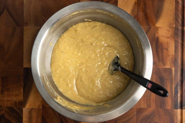 tahini banana bread batter in a metal mixing bowl set on a wooden cutting board.