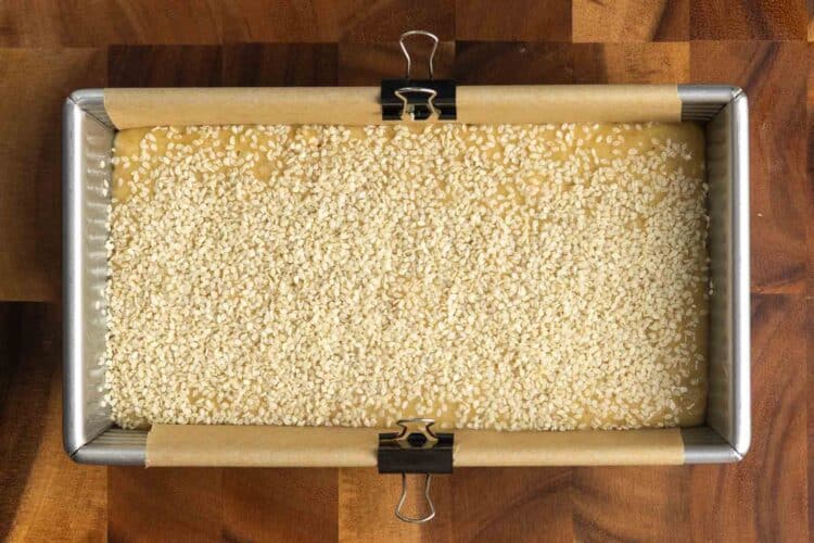 Banana bread batter in a parchment lined loaf pan, topped with white sesame seeds.