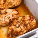Juicy oven baked chicken breasts resting in a baking dish with pan juices and golden seasoned crust
