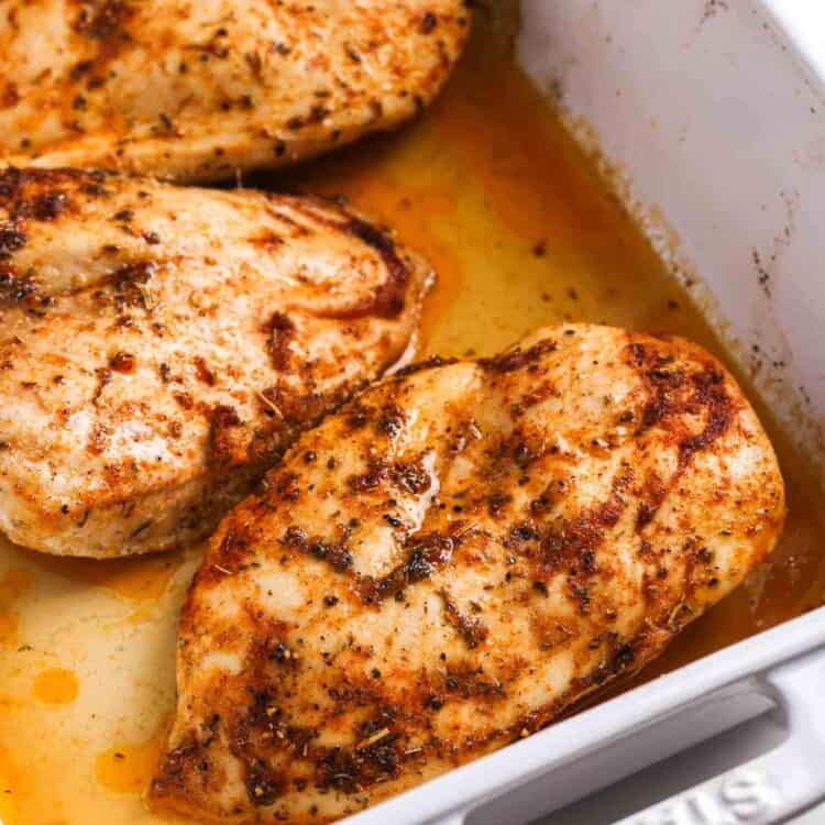 Juicy oven baked chicken breasts resting in a baking dish with pan juices and golden seasoned crust