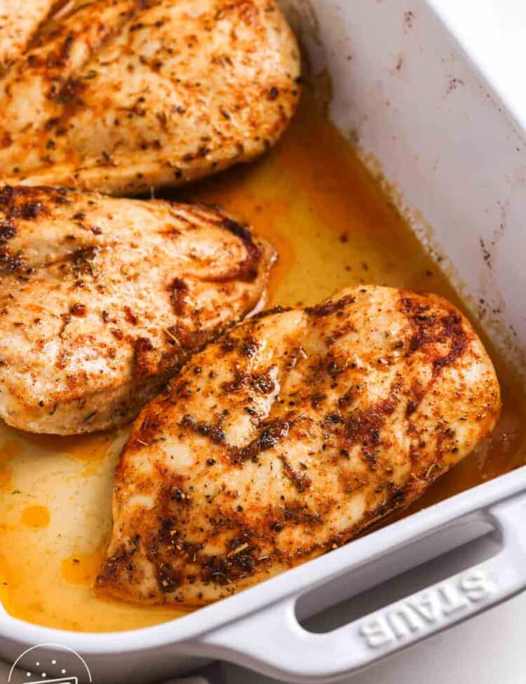 Juicy oven baked chicken breasts resting in a baking dish with pan juices and golden seasoned crust