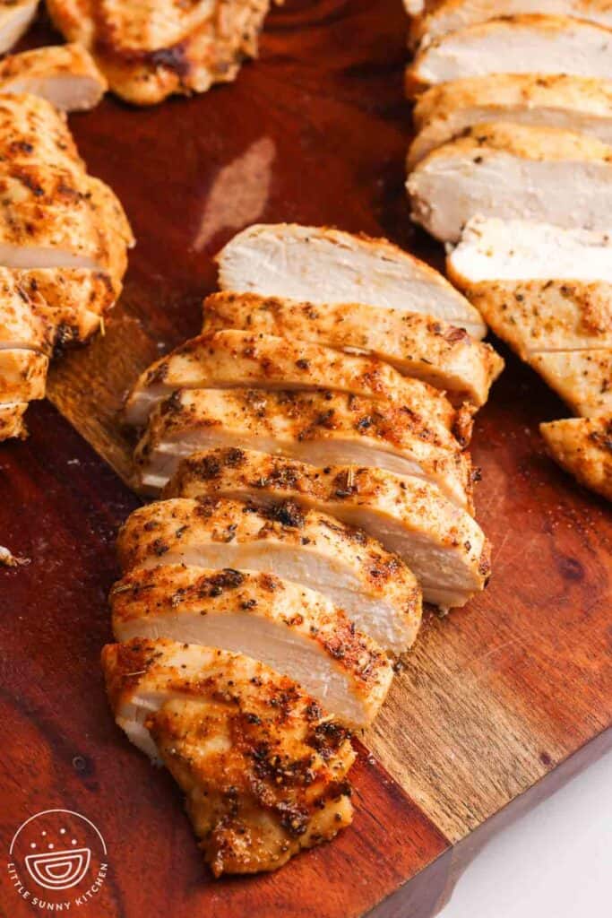 Sliced oven baked chicken breasts on a wooden cutting board with a seasoned golden exterior