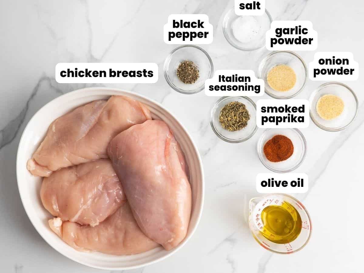 Ingredient shot for baked chicken breast with raw chicken breasts, olive oil, salt, ground black pepper, Italian seasoning, smoked paprika, garlic powder, and onion powder on a marble surface