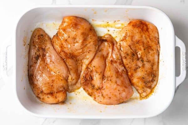 raw seasoned chicken breasts arranged in baking dish before baking
