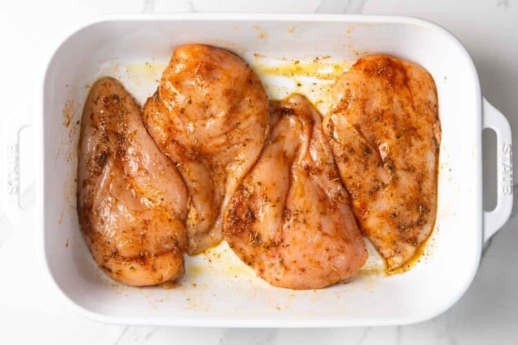 raw seasoned chicken breasts arranged in baking dish before baking