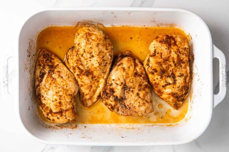 juicy oven baked chicken breasts resting in baking dish with pan juices