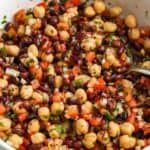Close up of balela salad in a white bowl made with chickpeas, black beans, diced tomatoes, finely chopped onion, fresh herbs, and sumac tossed in a lemon and olive oil dressing.