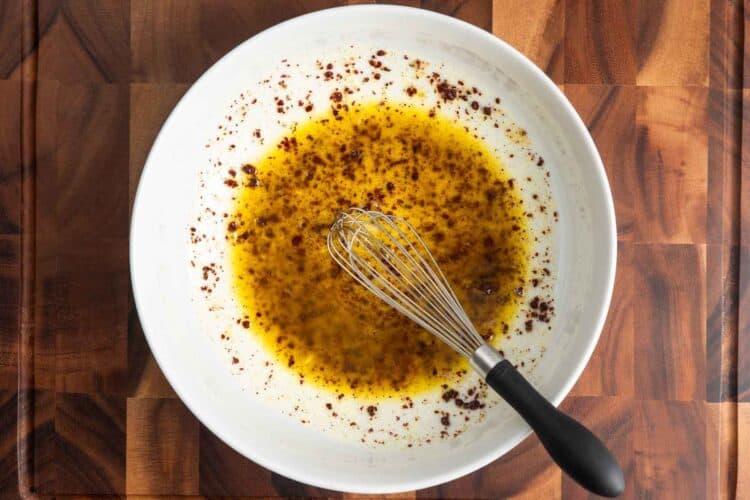 Lemon juice, extra virgin olive oil, garlic, and sumac whisked together in a white bowl to make the balela dressing.