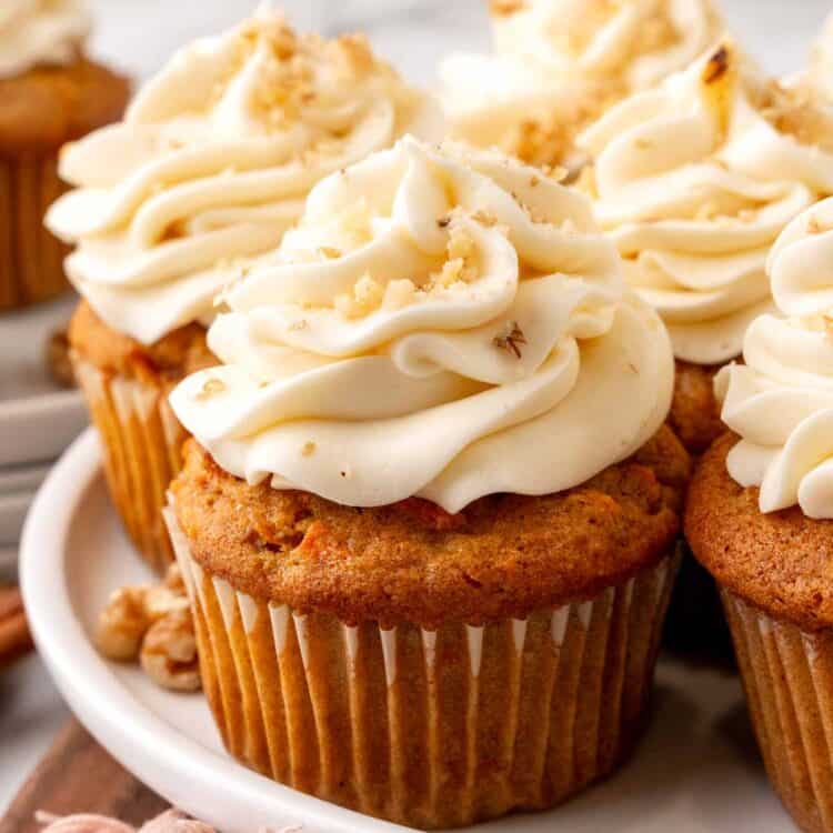 a plate of carrot cake cupcakes with cream cheese frosting, sprinkled with finely chopped walnuts.