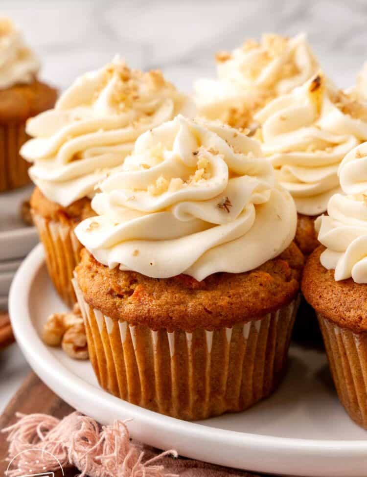 a plate of carrot cake cupcakes with cream cheese frosting, sprinkled with finely chopped walnuts.