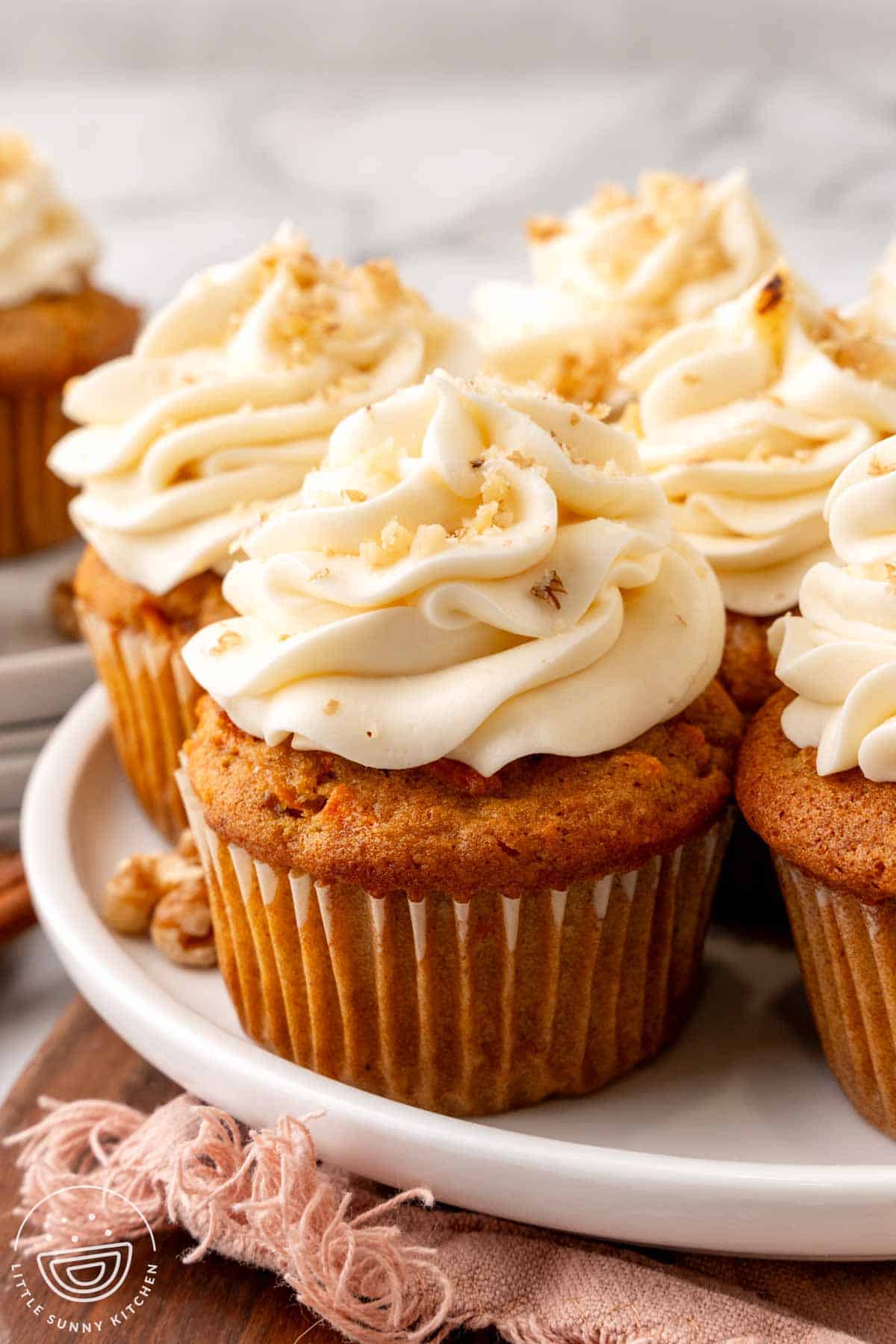 a plate of carrot cake cupcakes with cream cheese frosting, sprinkled with finely chopped walnuts.
