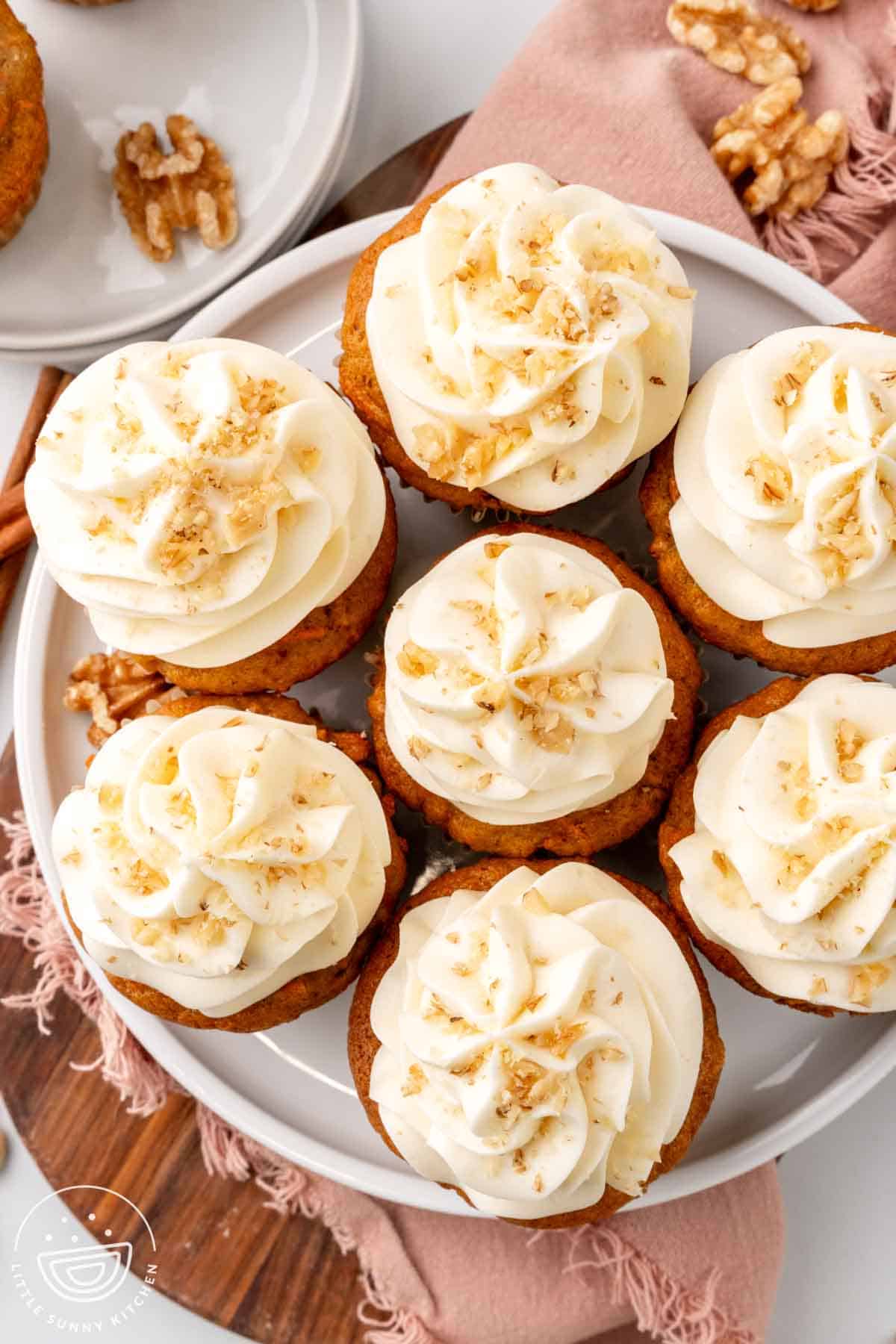 overhead view of a round plate holding 7 carrot cake cupcakes topped with cream cheese frosting.