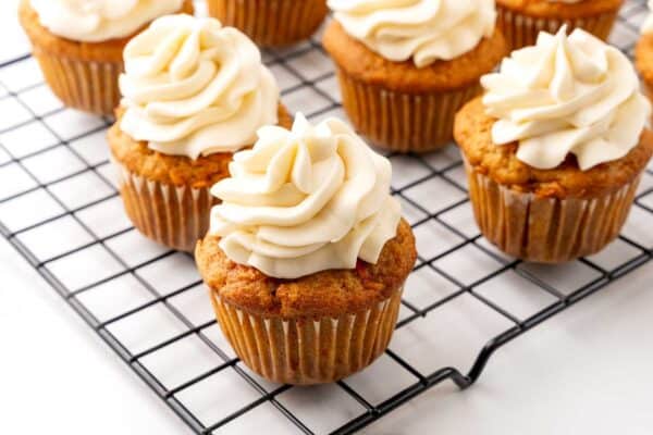 carrot cake cupcakes on a rack, topped with a swirl of cream cheese frosting.