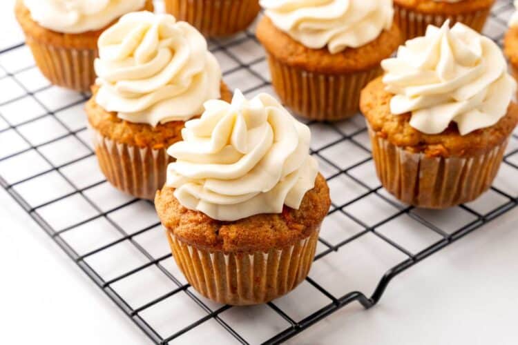 carrot cake cupcakes on a rack, topped with a swirl of cream cheese frosting.