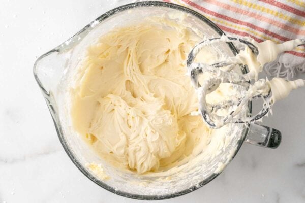 cream cheese frosting in a glass mixer bowl with the beaters above it.