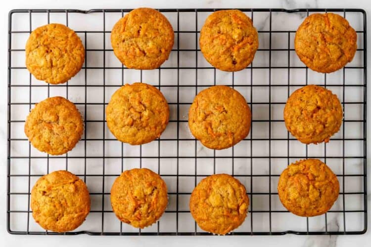 12 baked carrot cake cupcakes, cooling on a black wire rack.
