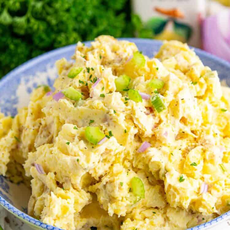 Close up of creamy smashed potato salad in a blue serving bowl, made with tender gold potatoes, mayonnaise dressing, celery, and red onion, with fresh parsley sprinkled on top.